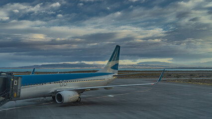 The plane is on the runway. The ladder is at the open door. Yellow marking lines on the asphalt. In the distance you can see a turquoise lake, a mountain range against the sky and clouds.