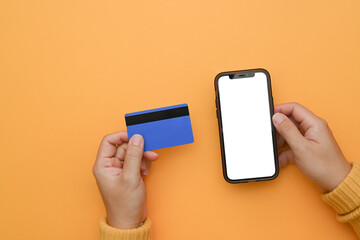 Woman hand holding mobile phone with blank screen and credit card on yellow background
