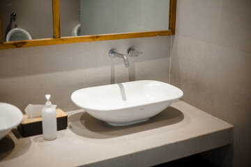 Modern white ceramic oval washbasin placed in bathroom near mirror with wooden frame and soap