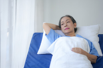 Elderly woman resting in a hospital bed, looking thoughtful. Patient in medical care. Bright and serene hospital room.