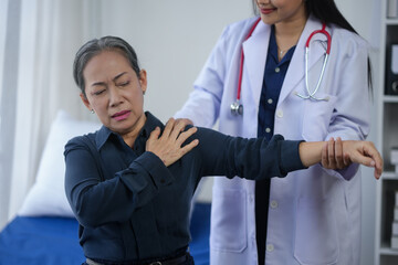 Senior woman experiencing shoulder pain during a medical examination with doctor in a clinic. Healthcare and patient care concept.