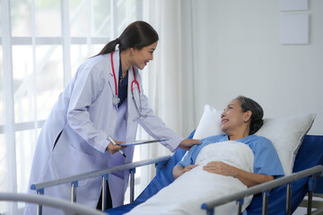 Smiling female doctor in white coat provides care and support to elderly patient lying in hospital bed, highlighting healthcare and compassion.