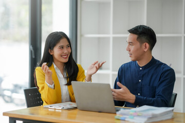 Two colleagues having a discussion in a modern office, using a laptop and documents, teamwork and collaboration concept.