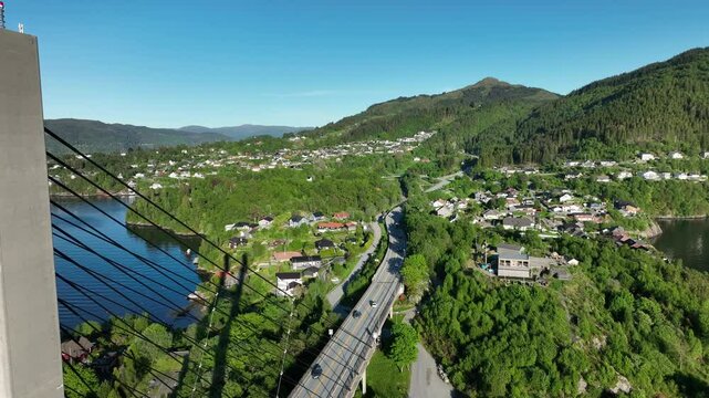 Drone passes close to Nordhordland Bridge tower, showcasing cables and structure. Below, the road leads to Mainland, Vagsgbotn and Bergen