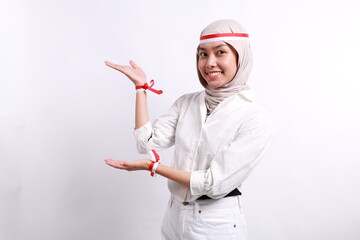 Excited Asian muslim woman wearing red white flag headband presenting at the copy space on the side. Independence day advertisement concept