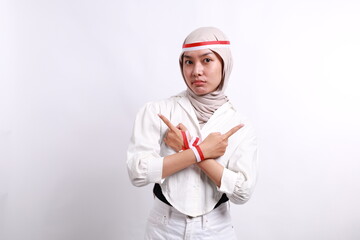 Confused young Asian muslim woman with red white ribbon for celebrating Indonesia independence day standing while pointing right and left side