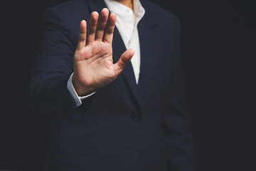 Fototapeta premium Businessman shows a stop gesture while standing on a black background.