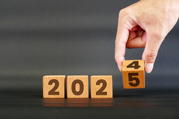 Hand flipping the years 2024 to 2025 on wooden cubes. Merry Christmas and New Year 2025 concept.