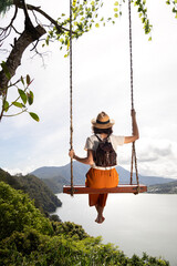 Young female tourist enjoying landscape sitting on a swing in Bali, Indonesia. Vertical image.