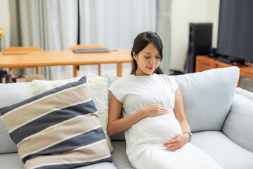 Pregnant woman sit on sofa and look at her tummy