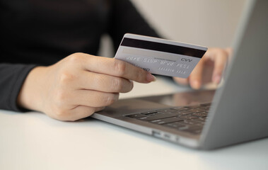 Asian girl shopping online holding credit and using laptop enter their card number in the mobile phone app to purchase and payment in internet store