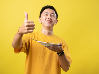 A young man in a yellow shirt is enthusiastically eating a plate of noodles with a fork against a...