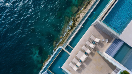 From the top of a skyscraper, the view encompasses a magnificent swimming pool with crystal-clear water and comfortable loungers, at a luxurious mansion beside the sea.
