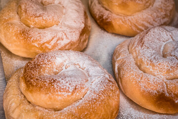 Close-up of fresh baked small Ensaimadas refined with powdered sugar on baking tray showcasing the traditional pork lard pastry product from Mallorca, perfect for highlighting local Mallorca desserts.