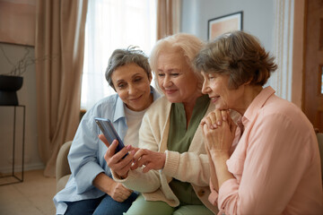 Smiling retired women friends looking on smartphone screen