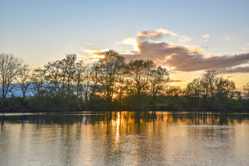 Serene sunset over a French river with calm waters reflecting clouds and shoreline trees