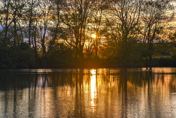 Serene sunset over a French river with calm waters reflecting clouds and shoreline trees