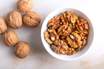 Walnuts in a white bowl on a marble plate. Shelled and dried halves of walnut kernels, ripe seeds of the common walnut tree Juglans regia, used as snack or for baking. Close-up from above, food photo.