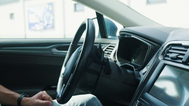 Self-parking vehicle using car park assistant park itself on sunny day. Male driver sitting inside and not touch steering wheel. Vehicle with advanced automotive technology