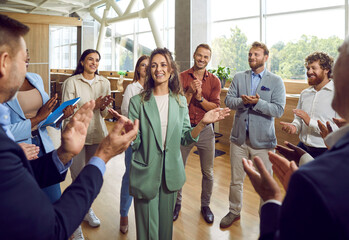 Group of company employees congratulating their happy female colleague on job well done applauding...