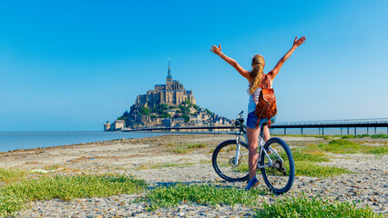 Happy woman tourist in bicycle enjoying view of Mont Saint Michel, France, Normandy