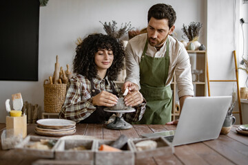 Two people in a pottery workshop crafting ceramic piece together. Collaborative art creation in...