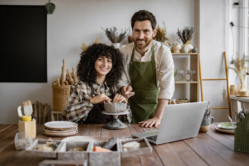 Smiling couple working together on pottery project in art studio. Creative process with laptop and...