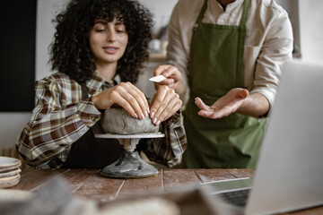 Female student learning pottery techniques from instructor in studio. Hands shaping clay on...