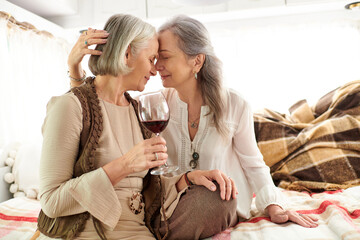 A lesbian couple shares a glass of wine while relaxing in their camping van.