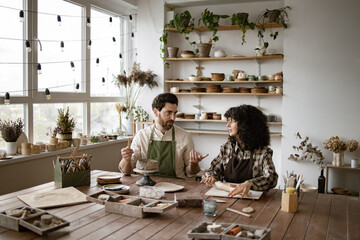 Bearded mature man and woman sculpting clay in ceramics studio. Man creating vase while woman rolls...