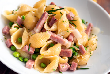 Piatto di pasta condita con prosciutto cotto, cipolla e pisellini, cibo italiano 