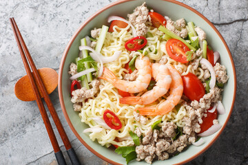Yum Mama Instant Ramen Noodle Salad with meat, shrimp and vegetables closeup on the plate on the marble table. Horizontal top view from above