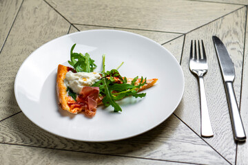 piece of pizza with smoked salmon and arugula on a white plate
