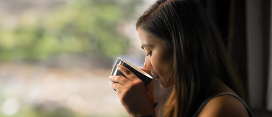 Indian young adult gen z girl sitting hold cup mug drink fresh hot coffee warm tea enjoy good morning day breakfast indoor home teen cheerful female lady relax rest spend break time room house