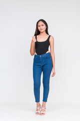 A young asian woman making thumbs up sign. Wearing a black bodysuit and jeans Isolated on a white background. Whole body photo.