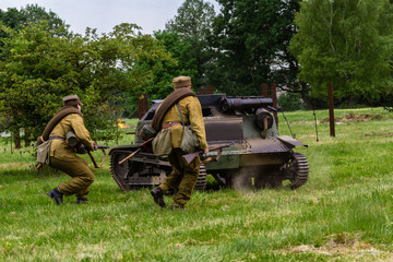 Fototapeta premium Historical reconstruction. Polish defensive war 1939. Battle of Wyry. Polish infantry soldiers fight on the battlefield under the cover of a tankette. View from the back. Wyry, Silesia, Poland