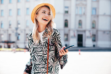 Young beautiful smiling blond hipster woman in trendy summer hippie costume clothes. Carefree female posing in the street. Positive model outdoors at sunset. Cheerful and happy, in straw hat