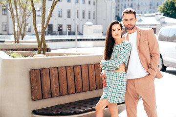 Fototapeta premium Beautiful fashion woman and her handsome elegant boyfriend in beige suit. Sexy brunette model in summer clothes. Fashionable smiling couple posing in street Europe. Brutal man and female outdoors