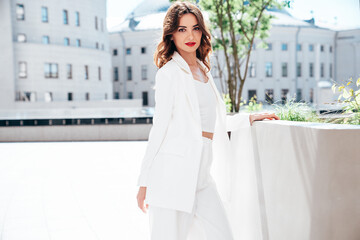 Fototapeta premium Young beautiful brunette woman wearing nice trendy white suit jacket. Sexy smiling model posing in the street at sunny day. Fashionable female outdoors. Cheerful and happy. Evening makeup, red lips