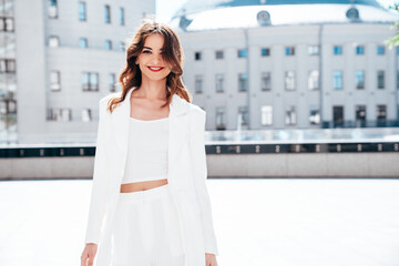 Young beautiful brunette woman wearing nice trendy white suit jacket. Sexy smiling model posing in the street at sunny day. Fashionable female outdoors. Cheerful and happy. Evening makeup, red lips