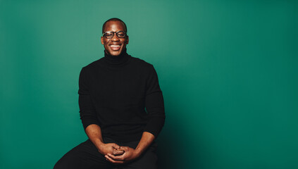 Stylish african man smiling in casual sweater and glasses on green background