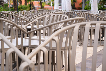A row of chairs are empty in a restaurant. The chairs are all the same color and are arranged in a neat row. The chairs are facing the same direction, and there are no people in the scene