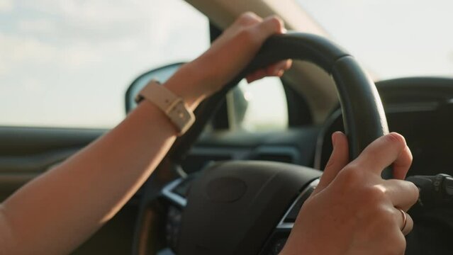 Close up view of female driver hands on steering wheel. Woman driving car at sunset. Inside view of modern vehicle moving on road