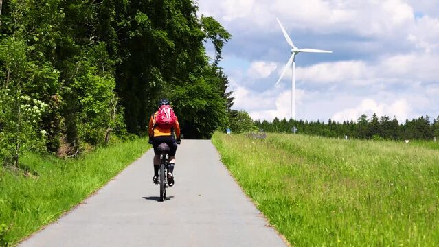 Cyclist Riding on a Cycle Path with a Wind Turbine in the Background