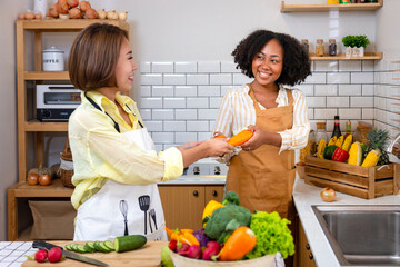 Asian woman and her African American friend is helping each other preparing healthy food with...