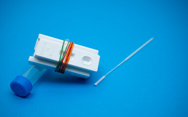 A few of Covid-19 rapid antigen test casettes tied with some rubber bands, with a nasal swab stick and a test tube; on blue background. A close-up and selective focus photo of the test cassette. 