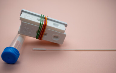 A few of Covid-19 rapid antigen test casettes tied with colorful rubber bands, with a nasal swab and test tube; isolated on pink background. A close-up and selective focus photo of the test cassette. 