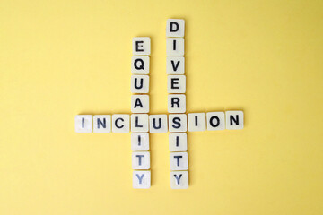 Text Equality, Inclusion and Diversity on Wooden Block Crossword Puzzle Over Yellow Background