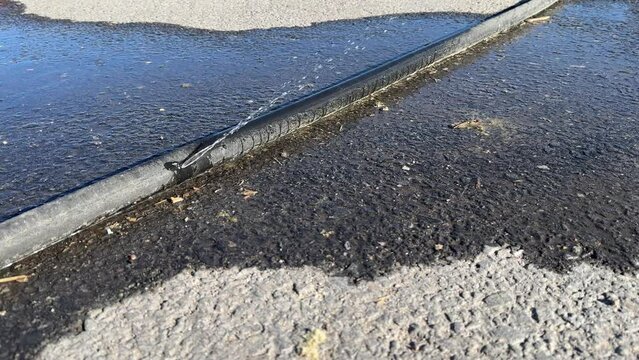 Leaking black polyethylene water pipe on ground outdoors