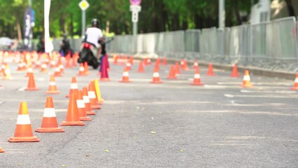 Unrecognizable people learn to drive a motorcycle by driving around plastic traffic cones during a driving lesson on a sunny summer day. Focus on the foreground.